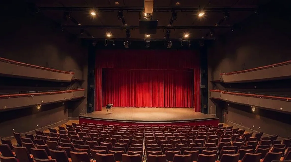Empty theatre with a red stage curtain and rows of seats